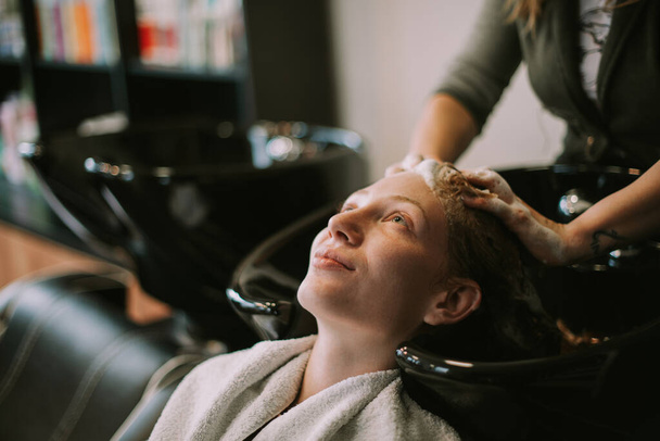 Крупный план парикмахера мыть своим клиентам рыжие волосы в парикмахерской - Фото, изображение