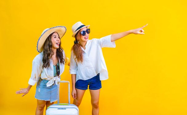 Two Pretty asian women passengers in trendy fashion is exciting to board while carrying her luggage bag in happiness for friendly trip and summer travel vacation isolated on yellow background - Photo, Image
