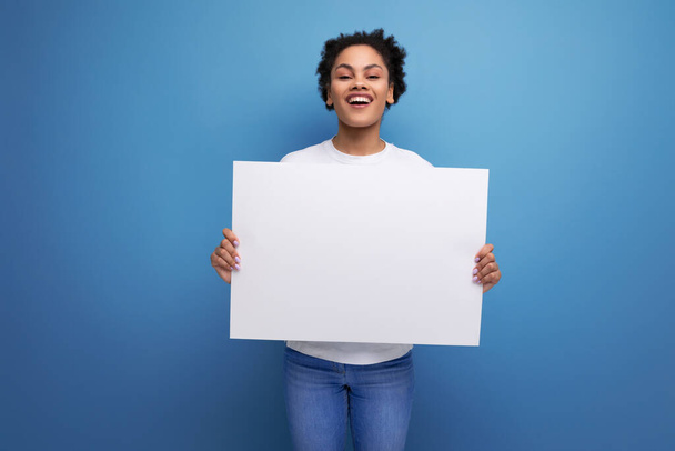 young pretty hispanic business music lover woman in a white t-shirt holding a white board with a mockup for advertising. - Photo, Image