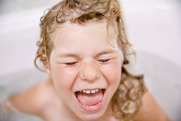Cute child with shampoo foam and bubbles on hair taking bath. Portrait of happy smiling preschool girl health care and hygiene concept. Washes hair by herself - Foto, Imagem