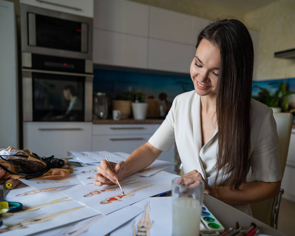 Woman drawing sketches of swimwear and underwear in watercolor while sitting in the kitchen - Foto, Bild