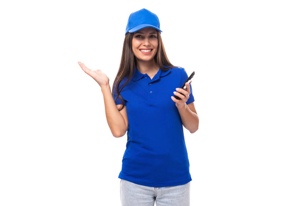 jong Kaukasisch brunette adverteerder vrouw in blank blauw t-shirt en pet met telefoon. - Foto, afbeelding