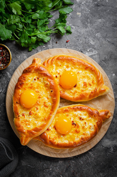 Ajarian Khachapuri, filled with cheese and topped with egg yolk, traditional Georgian Khachapuri with cheese-filled bread on Dark Rustic Background - Photo, Image