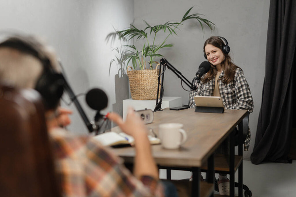 Pracownicy radia siedzą przy stole przed mikrofonami i razem nadają. Mężczyzna i kobieta w słuchawkach nagrywają podcast siedząc w studio. Wysokiej jakości zdjęcie - Zdjęcie, obraz