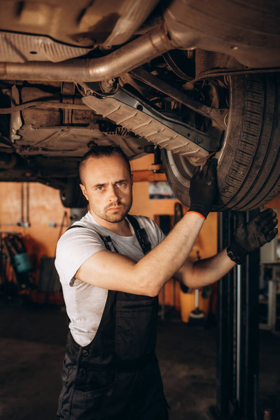 Portrait of a mechanic repairing a lifted car. - Фото, изображение