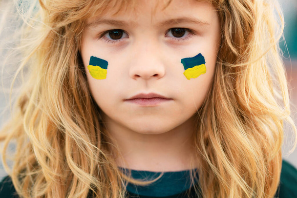 Sign of ukrainian flag on child cheek. Ukrainian geopolitics globe crisis. Close up kids face - Zdjęcie, obraz