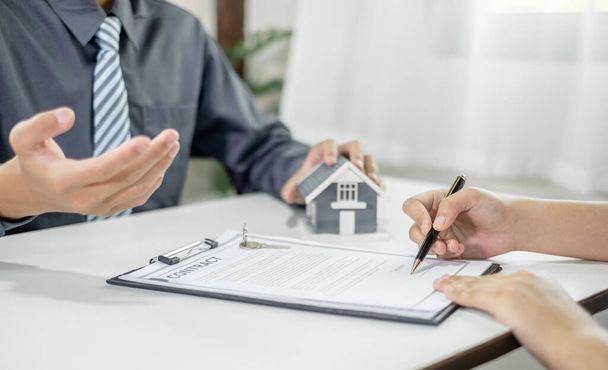 Ein Immobilienmakler mit einem Eigenheimmodell spricht mit Kunden über die Anmietung eines Hauses und den Kauf einer Hausversicherung und schließt den Vertrag nach Abschluss der formellen Verhandlungen ab.. - Foto, Bild
