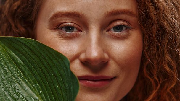 Beautiful redhead plus size woman with freckles holding green leaf isolated on blue background. Body positive. Cosmetology and skin care. - Photo, Image