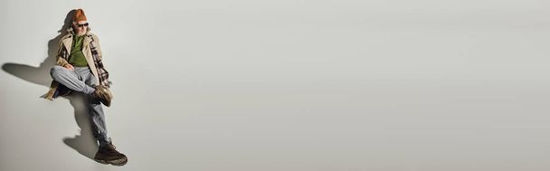 ausdrucksstarke Persönlichkeit, hochauflösende Ansicht eines älteren Hipstermannes in stilvoller Freizeitkleidung und dunkler Sonnenbrille auf grauem Hintergrund mit Schatten, modisches Alternskonzept, Banner mit Kopierraum - Foto, Bild