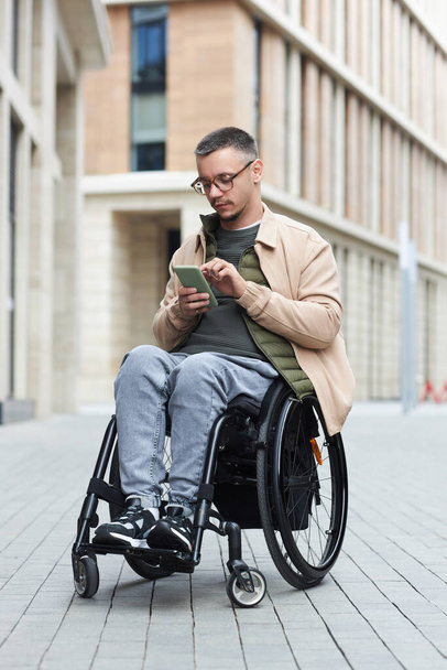Giovane con disabilità seduto sulla sedia a rotelle e messaggio di testo al telefono - Foto, immagini