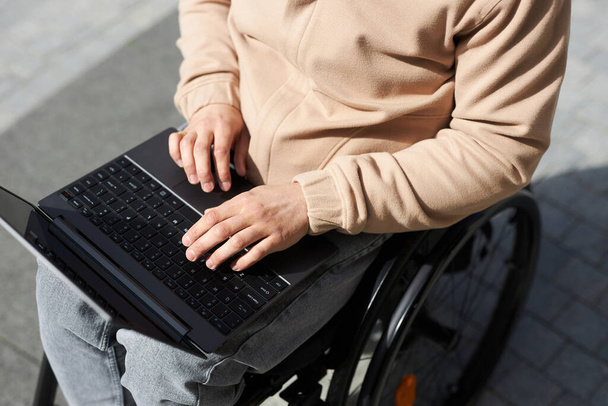 Visão de alto ângulo do jovem com deficiência digitando no laptop, ele trabalhando online ao ar livre - Foto, Imagem