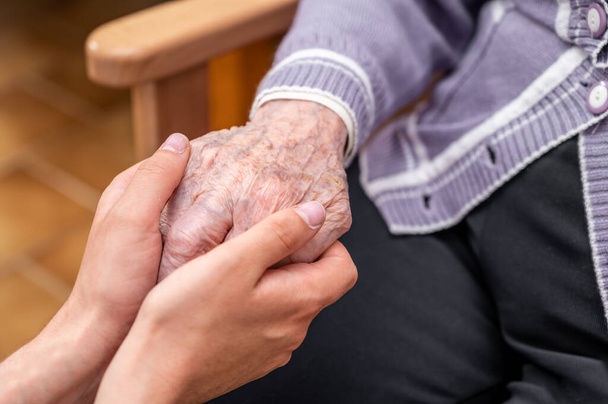 Close-up senior woman hand with her caregiver helping hands holding together, Caregiver visit at home. Home health care and nursing home concept. High quality photo - Photo, Image