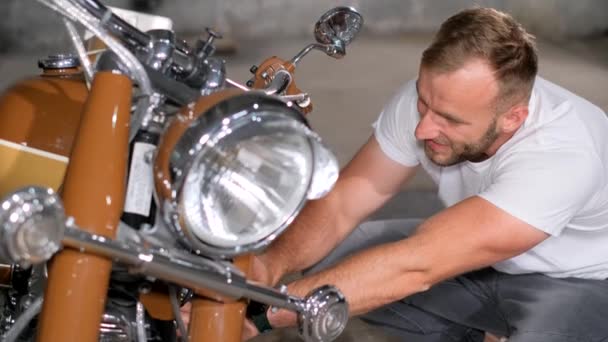Egy férfi szerelő megjavítja a motorját egy garázsban. Retro motorkerékpár szerviz. Függőleges videó - Felvétel, videó
