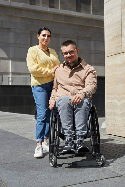 Imagen vertical del joven con discapacidad mirando a la cámara mientras camina con su amigo en la ciudad - Foto, imagen