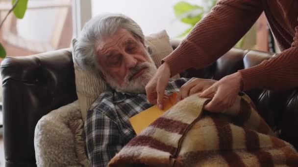 Un uomo anziano si addormentò sul divano leggendo un libro. Una moglie premurosa lo copre con una coperta. Filmati 4k di alta qualità - Filmati, video