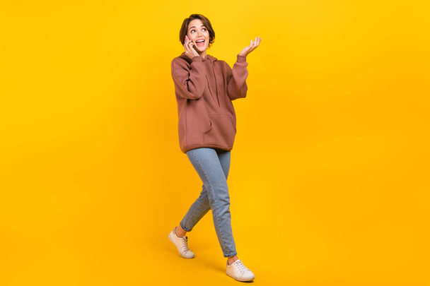 Full body profile photo of cheerful nice lady walking speak communicate telephone isolated on yellow color background. - Zdjęcie, obraz