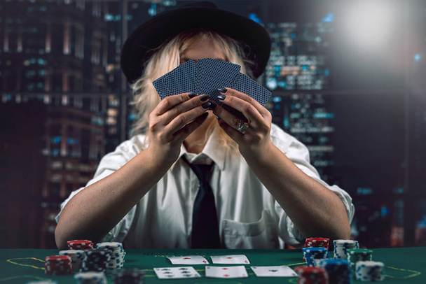 Mujer repartidor en sombrero con cartas y fichas de póquer en el casino viendo el juego. Repartidor de póquer. casino - Foto, Imagen