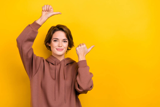 Portrait of promoter lady direct thumb fingers empty space novelty poster dressed hoodie shirt isolated yellow color background. - 写真・画像