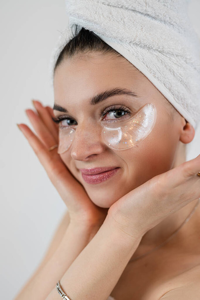 Donna caucasica toccare la pelle luminosa viso con macchie di idrogel sotto gli occhi isolati su bianco. Macchie oculari antirughe - Foto, immagini