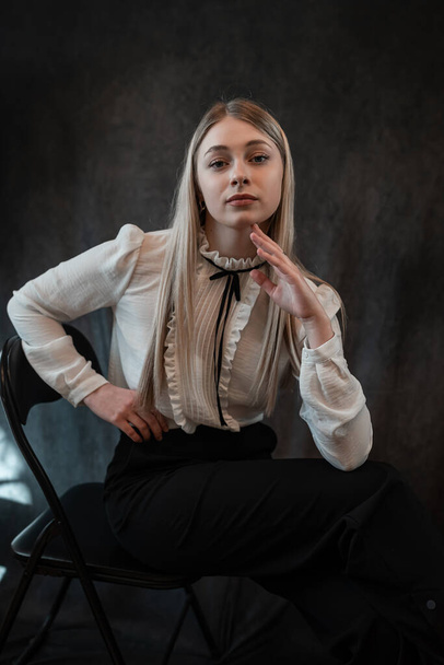 портрет улыбающейся блондинки позитивной деловой женщины носит белую блузку, сидящую на стуле, изолированную на черном. Стиль жизни - Фото, изображение