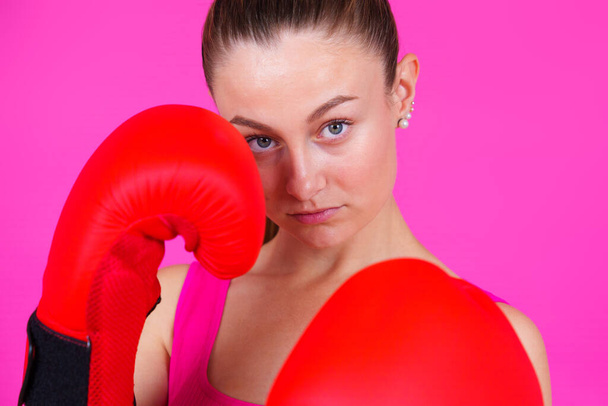 Portrét mladé ženy v boxerských rukavicích a při pohledu na fotoaparát izolované na růžovém pozadí. - Fotografie, Obrázek