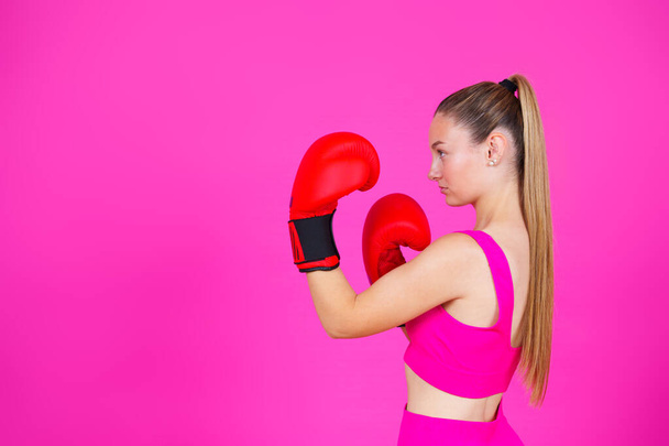 鮮やかなピンクの背景に隔離されたコピースペースを見てボクシング手袋を身に着けているスポーツ女性. - 写真・画像