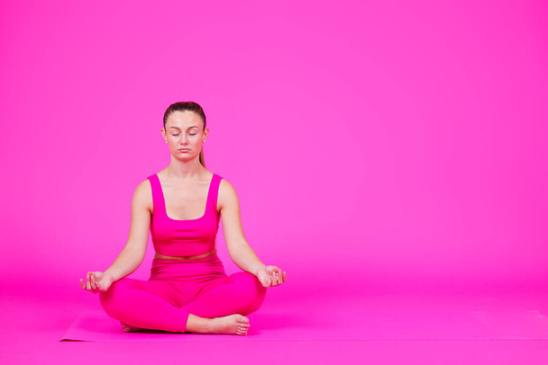 Młoda kobieta medytująca na podłodze, odizolowana na żywym różowym tle. Koncepcja zdrowia psychicznego z przestrzenią kopiującą. - Zdjęcie, obraz