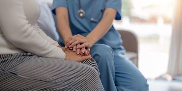 Doctor giving hope. Close up shot of young female physician leaning forward to smiling elderly lady patient holding her hand in palms. Woman caretaker in white coat supporting encouraging old person. - Photo, Image