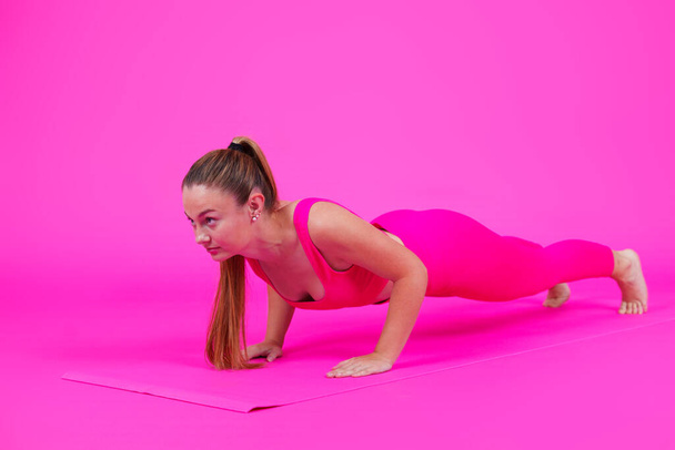Young sportswoman doing push-up exercise isolated on pink background. Concentrated woman doing exercise. - Foto, immagini