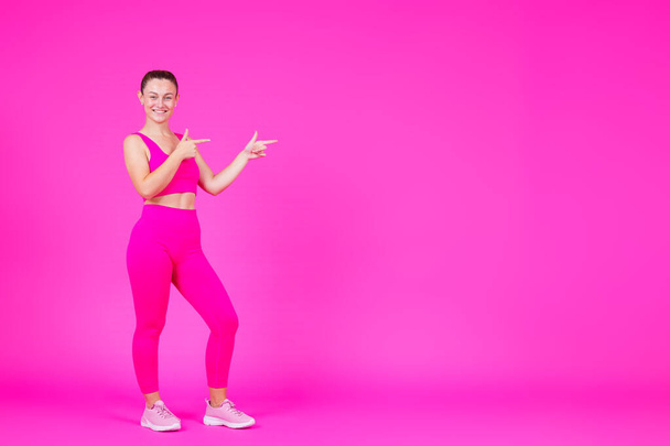 Plná délka sportovkyně ukazuje na růžové kopírovací místo. Fitness instruktor zobrazující zprávu izolované na pulzujícím pozadí - Fotografie, Obrázek