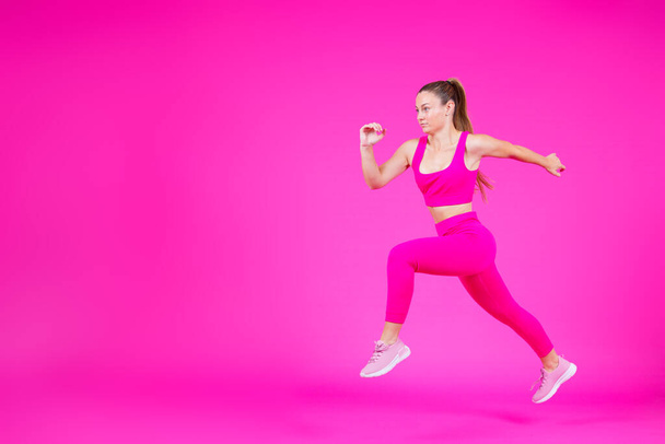 鮮やかなピンクの背景に隔離された実行しているスポーツ女性の完全な長さ。コピースペースで運動をする若い女性 - 写真・画像