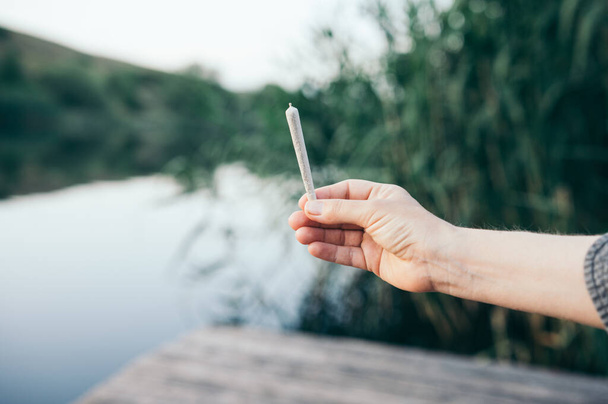 Cannabis joint man holding in his hand in nature smoking marijuana - Foto, afbeelding