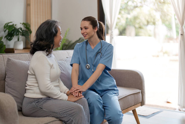 caregiver with senior woman and holding hands for care indoors. Retirement, consulting and professional female nurse with elderly person smiling together for healthcare support at nursing home. - Photo, Image
