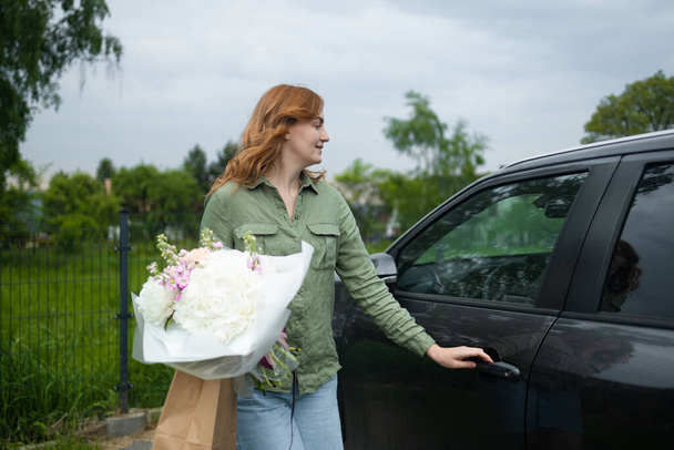 Arabasının yanında elinde güzel bir buket çiçekle çekici genç bir kadının portresi. - Fotoğraf, Görsel