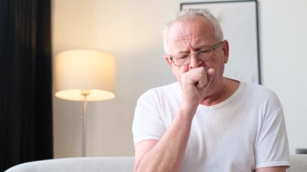 A sick elderly grandfather coughs while sitting on the sofa in an apartment without heating due to debt. Unhealthy sick elderly pensioner. - Filmmaterial, Video