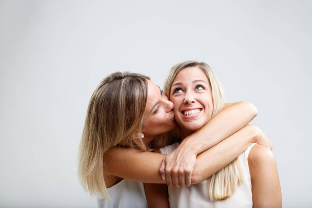 Kaksi blondi naiset vaihtaa hellä syleilee, hyväilee, ja poski suukkoja. Heidän siteensä heijastaa sisaruutta, kun he poseeraavat yhdessä hellästi. - Valokuva, kuva