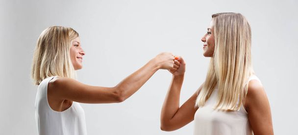 Deux blondes heureuses s'engagent dans une poignée de main spéciale, symbolisant leur forte amitié. Leurs cheveux longs et leurs vêtements légers sont remarquables - Photo, image