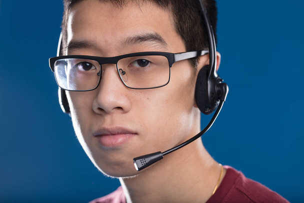 Asiático reflexivo y serio adulto con auriculares, típico de los jugadores o centros de llamadas, esperando para ayudar. El trabajo en equipo es clave en ambos campos - Foto, Imagen