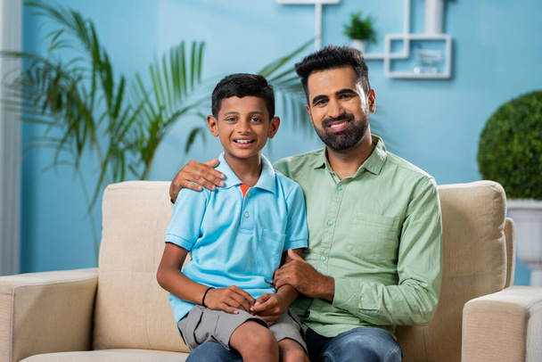 Boldog indiai apa fiával a kamerába néz, miközben otthon beszél - az apaság, a nevelés és a felelősség fogalma. - Fotó, kép
