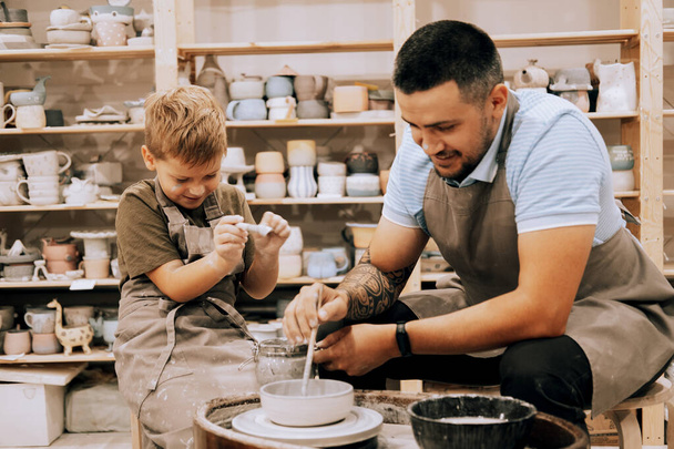 Pottering with son. Confident young man and little boy making ceramic pot on the pottery class. Lifestyle concept. - Фото, зображення