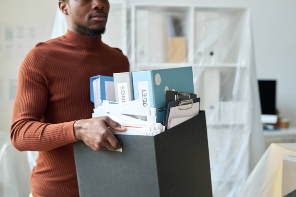 African American man carrying box with folders during movement in new office - Foto, imagen