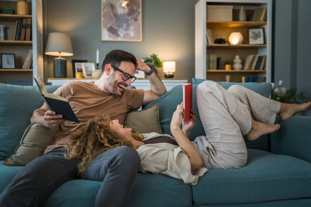 Coppia di adulti uomo e donna marito e moglie caucasici in una relazione libro reale tenere libri sul divano letto a casa in appartamento lettura tempo libero legame concetto di famiglia persone reali copiare spazio - Foto, immagini