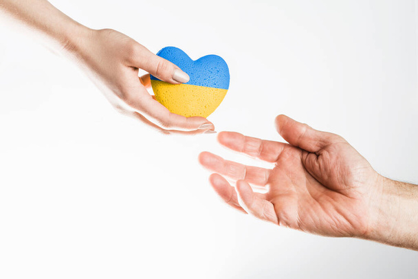 Naiskäsi antaa sinistä keltaista ukrainalaista sydäntä miespuoliselle kädelle kevyellä taustalla. konsepti tarvitsee apua ja tukea, totuus voittaa - Valokuva, kuva