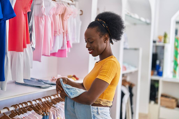 Afroamerikanerin Verkäuferin hängt Kleidung an Kleiderständer in Bekleidungsgeschäft - Foto, Bild