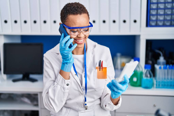 Científica afroamericana hablando en un smartphone buscando muestra en laboratorio - Foto, Imagen