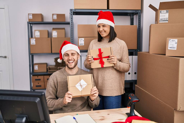 Dwoje młodych ludzi pracujących w małym biznesie e-commerce na Boże Narodzenie mrugających oczami przed kamerą z seksowną ekspresją, radosną i szczęśliwą twarzą.  - Zdjęcie, obraz