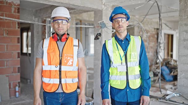 Two men builders standing together with relaxed expression at construction site - Fotoğraf, Görsel