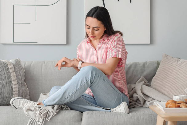 Молода жінка зі стильним наручним годинником сидить на дивані вдома
 - Фото, зображення