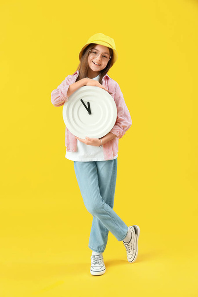 Little girl with wall clock on yellow background - Photo, Image