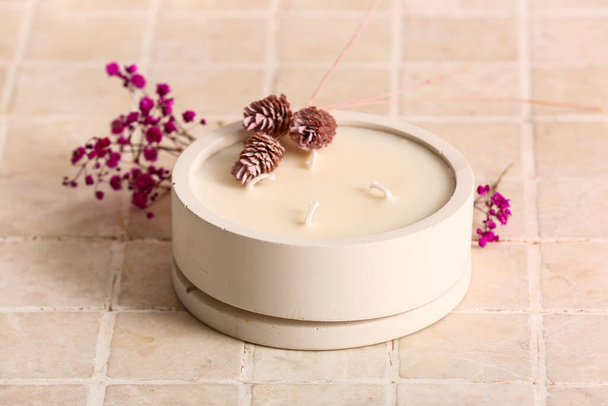 Soporte con vela y flores sobre fondo de baldosa beige - Foto, Imagen
